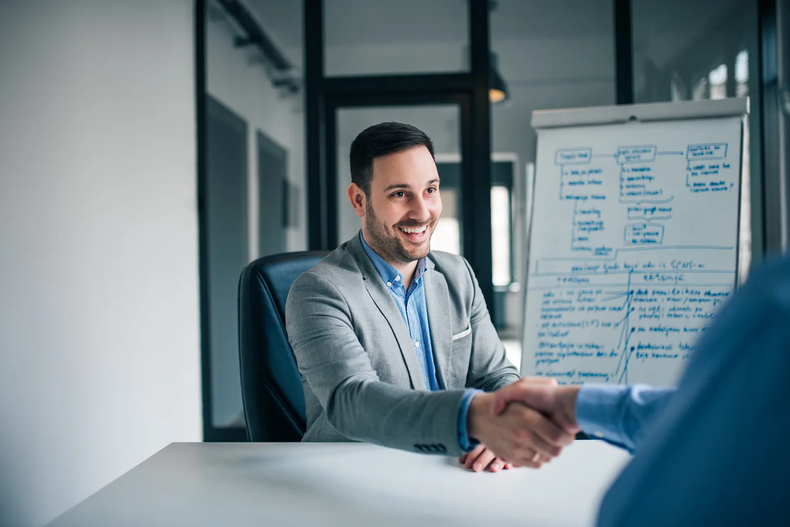 A broker shaking hands with a client across a meeting table